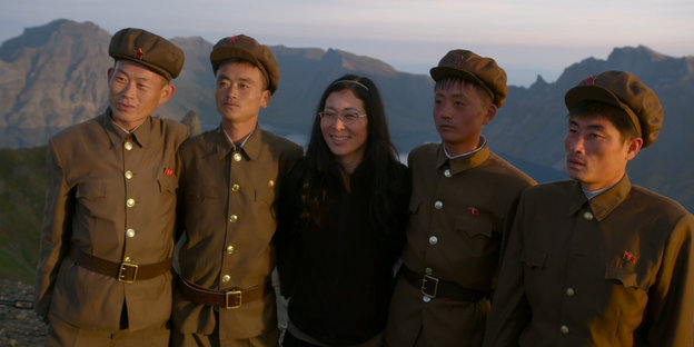 Frau mit Brille mit Militärs in Uniform vor Bergkette