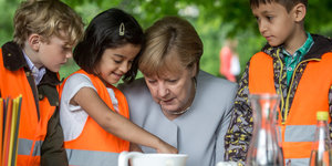 Angela Merkel umringt von Kindern vor einem Tisch mit Gläsern und Kolben