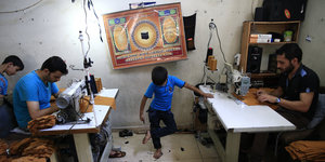 Syrische Männer an Nähmaschinen, dazischen steht ein kleiner Junge