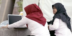 Zwei Frauen mit Kopftuch sitzen vor einem Laptop