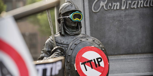 Ein Mann mit Rüstung, Schwert und Taucherbrille hält ein TTIP-Verbotsschild hoch.