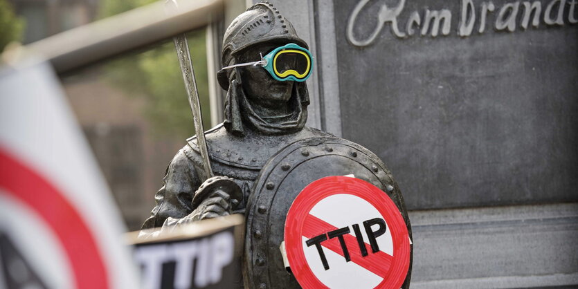 Ein Mann mit Rüstung, Schwert und Taucherbrille hält ein TTIP-Verbotsschild hoch.