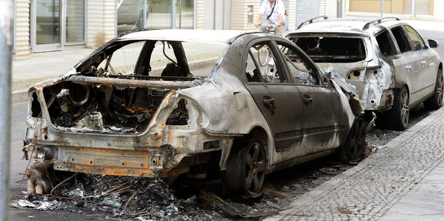 Ein ausgebranntes Autowrack und ein vom Brand beschädigtes Fahrzeug