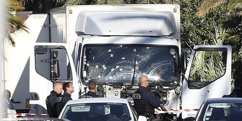 Ein Lkw mit Einschüssen in der Frontscheibe steht hinter anderen Autos. Sicherheitskräfte stehen davor.