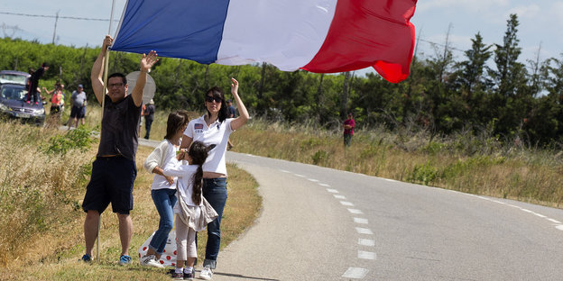 Menschen halten die französische Nationalflagge, während sie am Straßenrand stehen