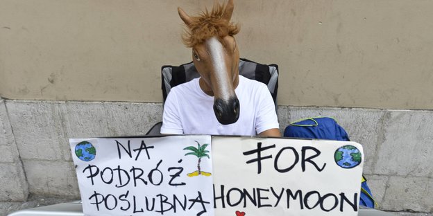 Ein Mann mit Pferdemaske auf dem Kopf spielt auf einem Piano. Auf einem Schild vor ihm steht auf polnisch und englisch "for Honeymoon"