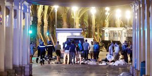 Sicherheitsleute stehen am Tatort in Nizza, am Boden liegen zugedeckte Leichen