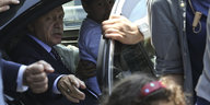 Recep Tayyip Erdogan sitzt in einem Auto, die Tür ist offen und er deutet mit der Hand hinaus