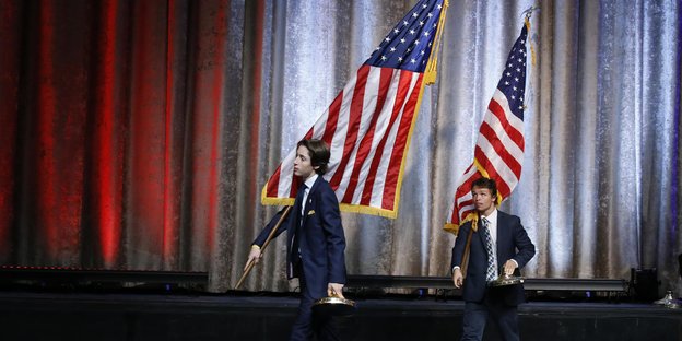 Zwei jungen Männer tragen US-Flaggen von einer Bühne