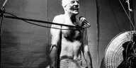 Ein Mann mit nacktem Oberkörper und bandagiertem Kopf vor einem Mikrophon