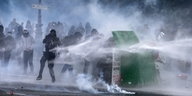 Demonstranten schützen sich vor den Strahlen eines Wasserwerfers, in dem sie sich hinter einem Müllcontainer verbergen