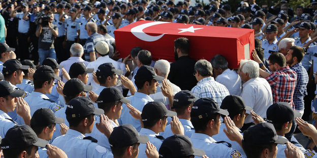 Polizisten salutieren vor einem Sarg, auf dem eine türkische Fahne liegt