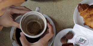 Zwei Hände halten eine leere Kaffeetasse, rechts ein Croissant