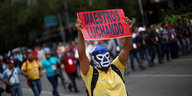 Ein Demonstrant trägt eine Wrestlingmaske des Lucha Libre und hält ein Schild hoch, auf dem „Maestros Luchando“ steht