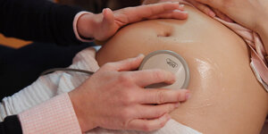 Eine Hand positioniert eine CTG-Sonde auf dem Bauch einer Schwangeren