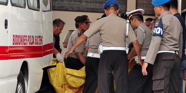 Indonesische Polizisten tragen zwei MIT-Terroristen in Planen vom Krankenwagen ins Krankenhaus