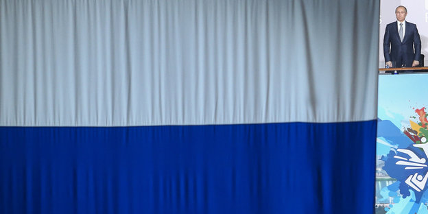 Waldimir Putin steht neben einer riesigen russischen Fahne