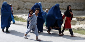 Eine Gruppe Menschen, teilweise in blauen Burkas verhüllt gehen eine Straße entlang