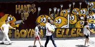 Menschen vor einem Wandbild in Istanbul, auf dem eine Figur andere mit einer Waffe bedroht