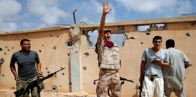 Libyscher Kämpfer vor einer zerschossenen mauer in Sirte