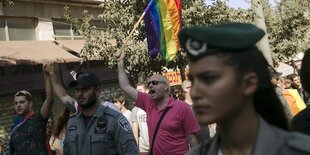 Eine Polizistin läuft neben Pride-Teilnehmer_innen. Einer hält eine Regenbogenfahne in die Höhe