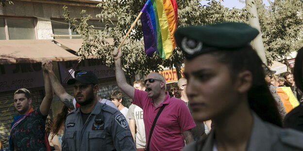 Eine Polizistin läuft neben Pride-Teilnehmer_innen. Einer hält eine Regenbogenfahne in die Höhe