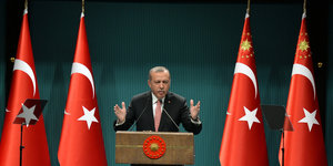 Mann in Anzug an Rednerpult, daneben türkische Fahnen. Es ist der türkische Präsident Erdogan