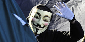 Ein Mann mit Anonymous-Maske winkt in die Kamera