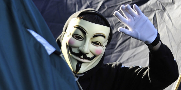 Ein Mann mit Anonymous-Maske winkt in die Kamera