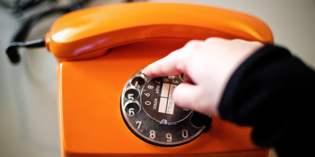 Eine Hand bedient die Wählscheibe eines alten orangefarbenen Telefons