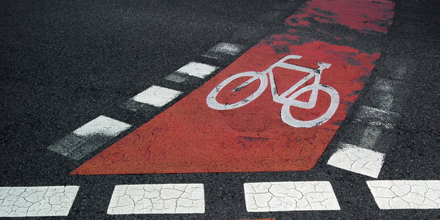 Ein weißes Fahrrad auf rotem Grund ist auf den Asphalt gemalt