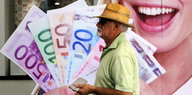 Ein Mann läuft an einem Werbeplakat vorbei, dass eine Hand mit Geldscheinen darin zeigt