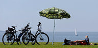 Auf einer Wiese stehen zwei Fahrräder, daneben ein Sonnenschirm und ein liegender Mensch
