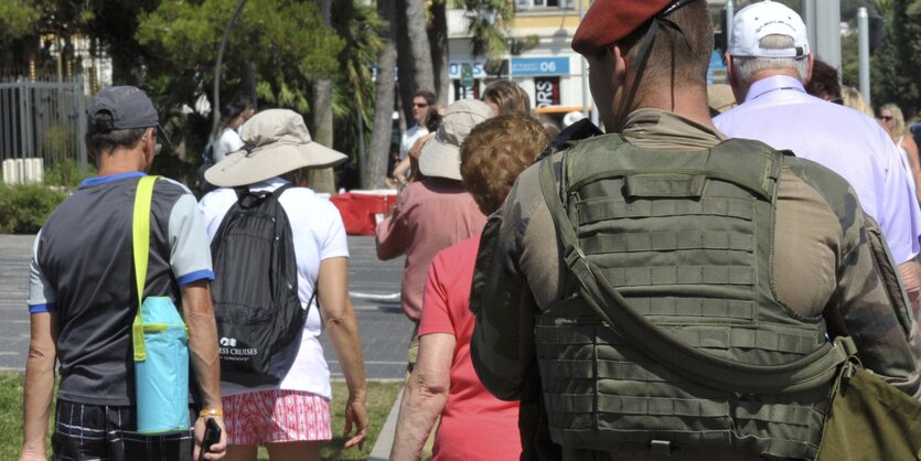 Ein französischer Soldat, schwer bewaffnet, läuft zwischen Urlaubern