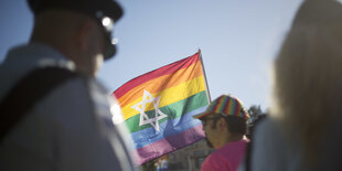 Ein Polizist, schräg dahinter ein Mensch mit einer Regenbogenfahne