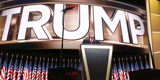Donald Trump steht vor vielen Fahen und einem riesigen Schriftzug mit seinem Namen auf der Bühne in Cleveland