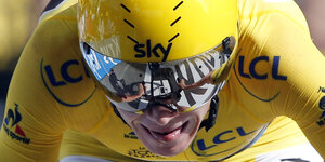 Ein Rennradfahrer in gelber Radmontur mit verspiegelter Sonnenbrille streckt die Zungenspitze aus dem Mund
