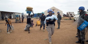 Blauhelme und Zivilisten tragen ein Baby und Gegenstände