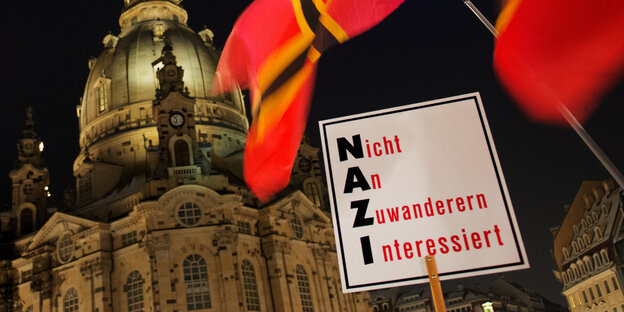 Vor der Frauenkirche in Dresden wird ein Schild hochgehalten auf dem steht „Nicht an Zuwanderern interessiert“. Die Anfangsbuchstaben der Worte sind gefettet