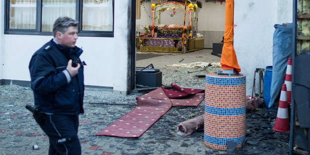 ein Polizist läuft an einem Gebetshaus von Sikhs vorbei, in dessen Eingangsbereich Scherben liegen