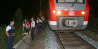 Nacht, stehender Zug auf Gleis, daneben Polizisten und Zivilisten