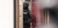 Ein Polizist guckt mit einem Maschinengewehr hinter einer Wand vor