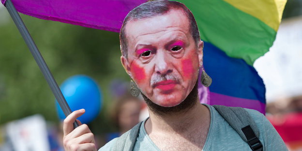 Eine Person mit einer Erdogan-Maske hält eine Regenbogenflagge in der Hand