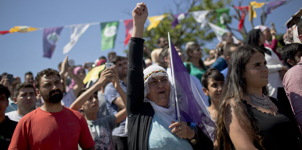 DemonstrantInnen stehen nebeneinander. Eine Frau mit Kopftuch reckt die Faut in die Höhe