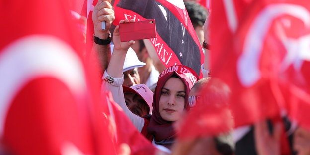 Eine Frau hält ein Smartphone in die Höhe. Um sie herum wehen türkische Fahnen.
