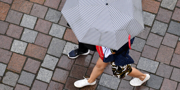 Aus der Vogelperspektive: Zwei Menschen Laufen über Pflastersteine. Sie sind mit einem Regenschirm geschützt.