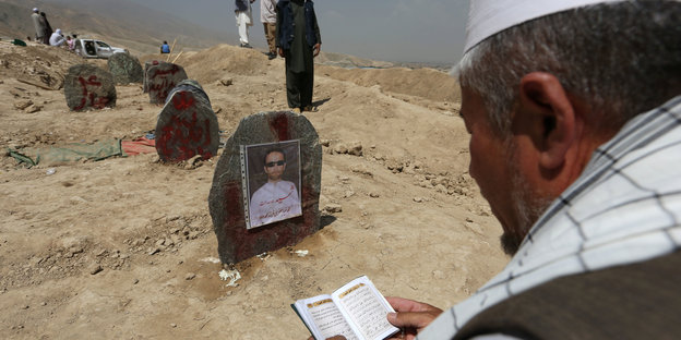 Mann mit Gebetsbuch vor einer Reihe von Grabsteinen