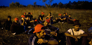 Mehrere Männer sitzen bei Dunkelheit im Gras
