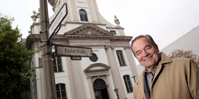 Ein Mann im Trenchcoat steht vor einer Kirche