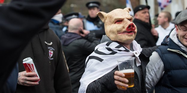 Ein Mann mit Schweinsmaske und Bier auf einer Demonstration